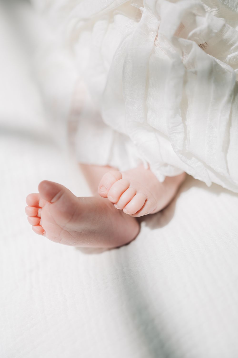 Close-up of tiny baby feet against white fabric in soft natural light.