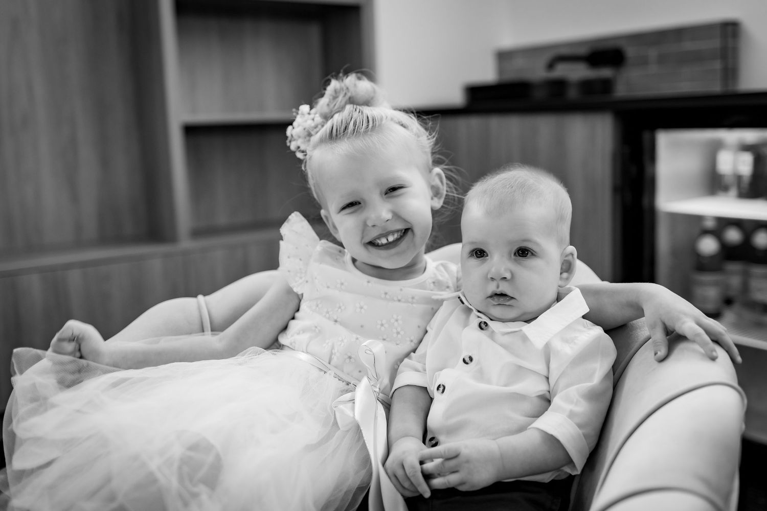 Black and white portrait of two children sharing tender moment on couch.