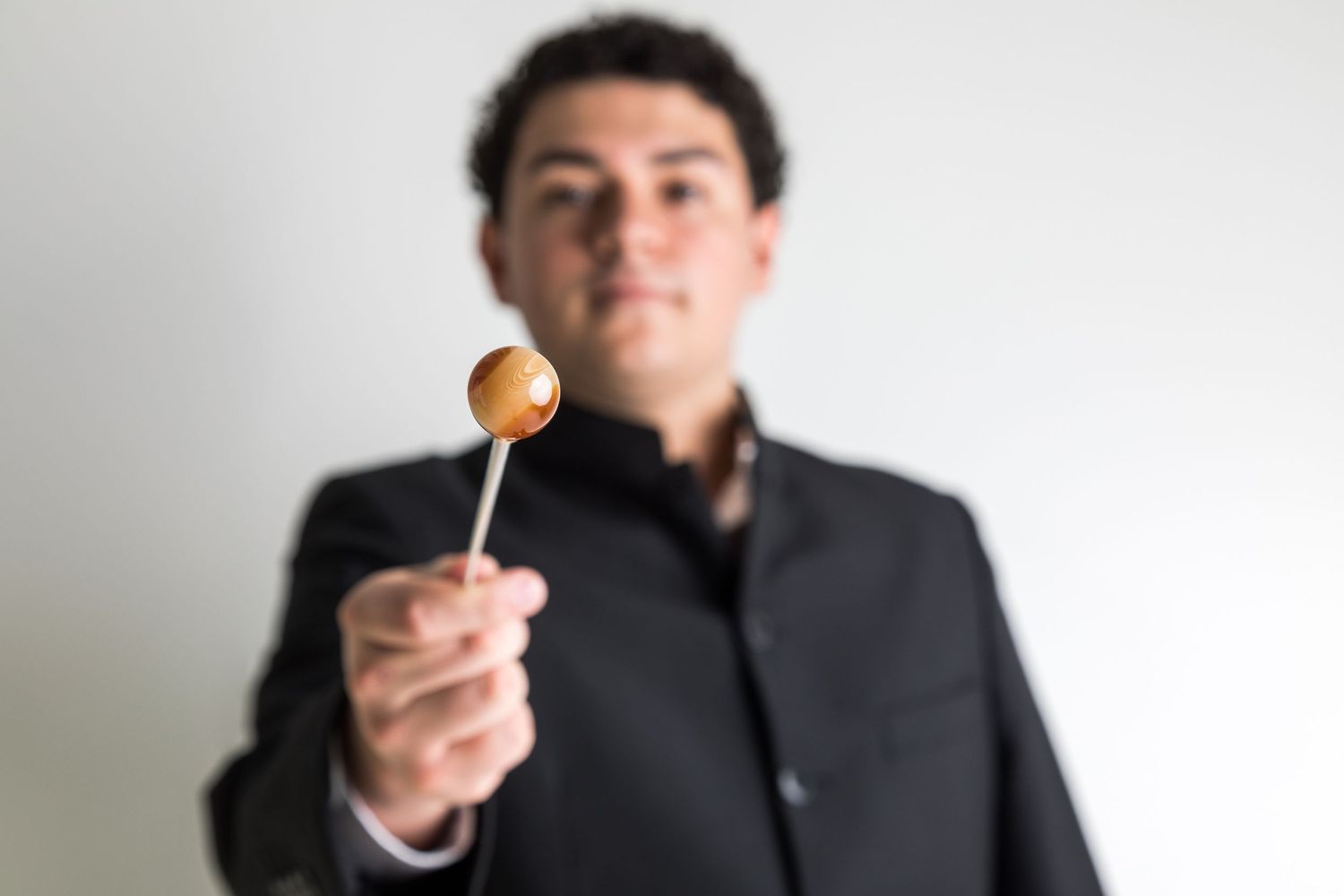 Conductor in dark jacket holds up a small lollipop with playful expression.