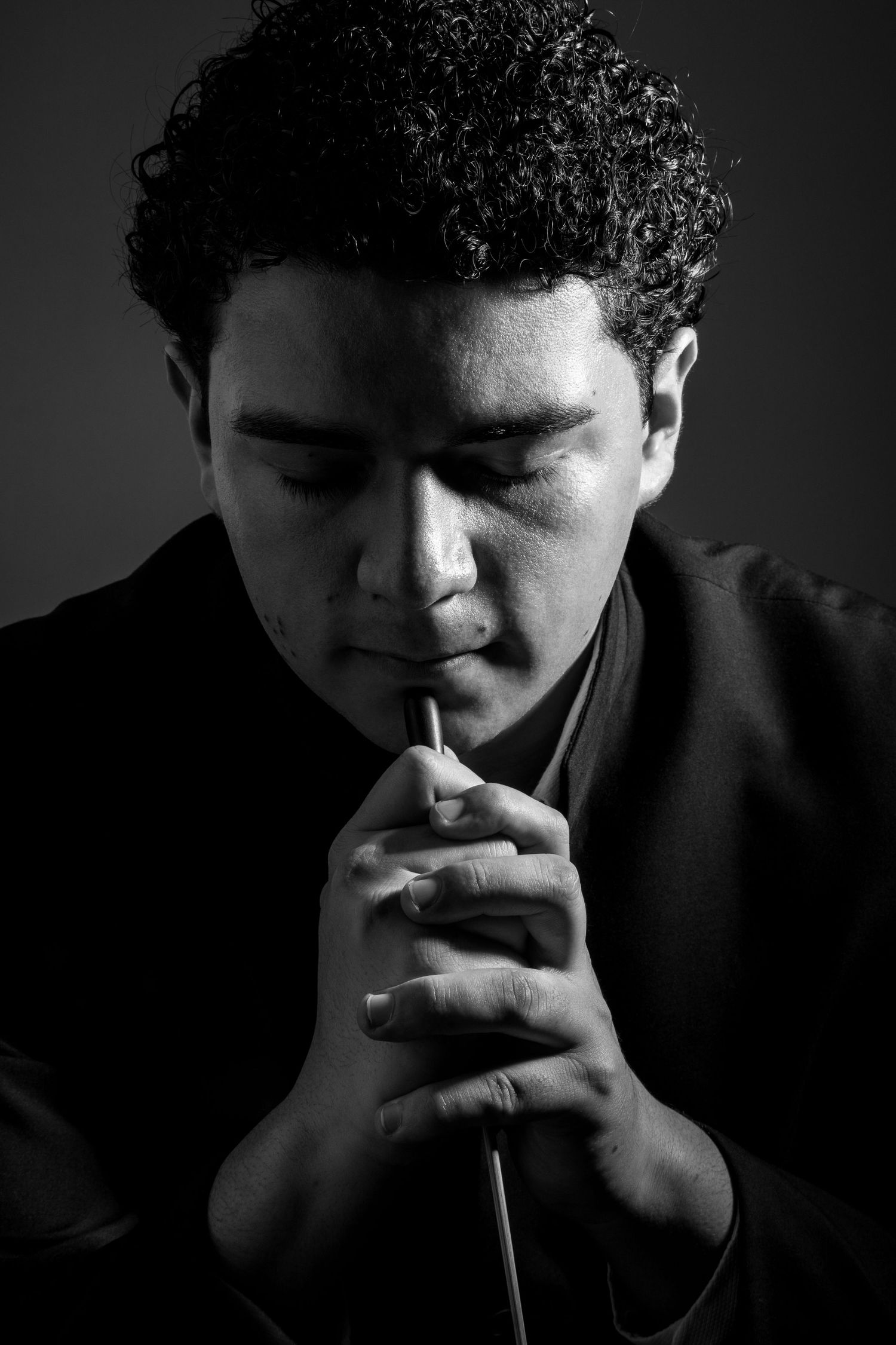 Conductor in contemplative pose holding baton in moody black and white portrait.