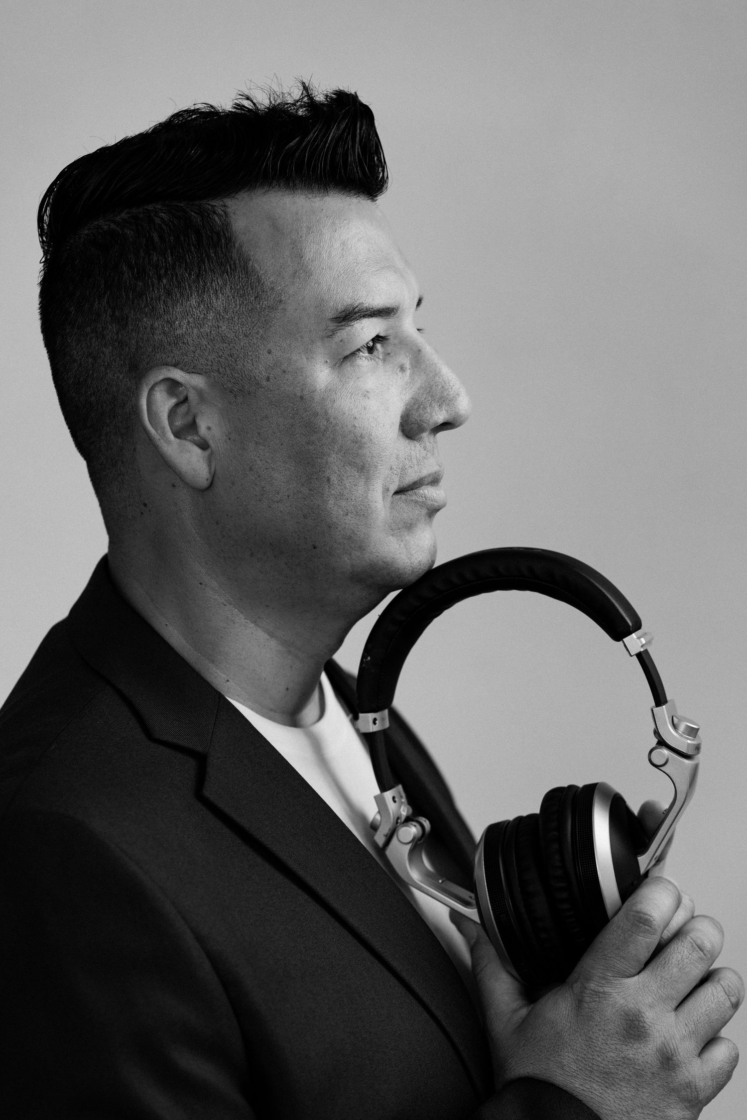 Black and white profile portrait of a man in a suit holding professional headphones against a light background.
