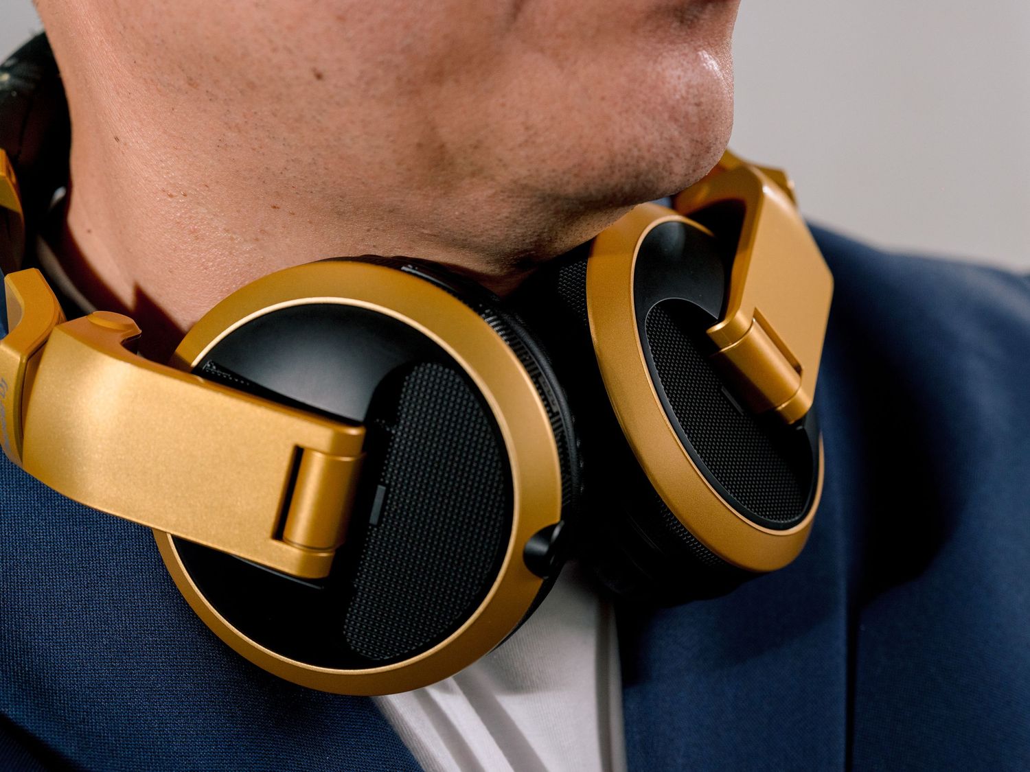 Gold and black over-ear headphones resting around a man's neck wearing a blue suit jacket.