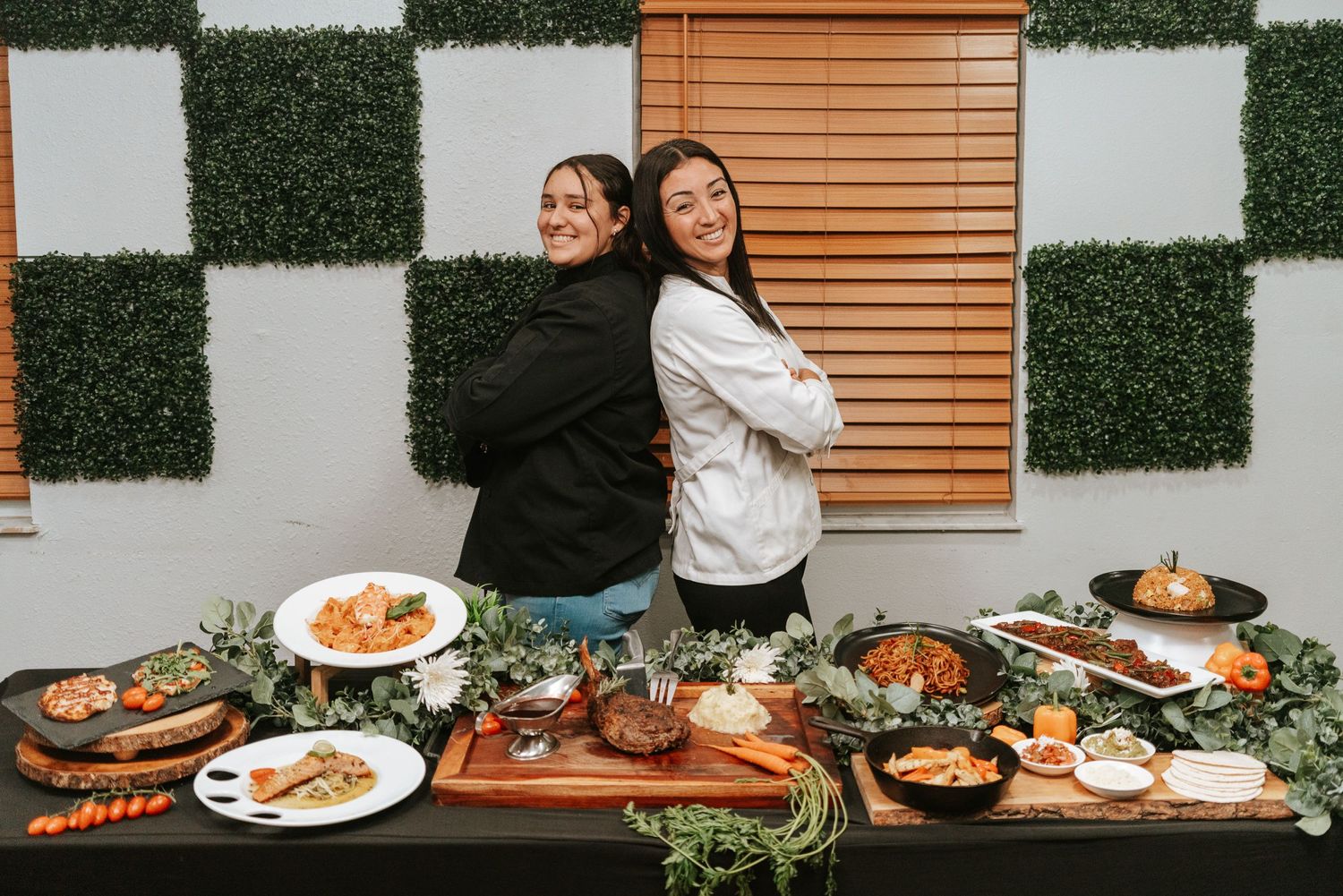Catering display with elegant food spread and decorative greenery against checkered wall.