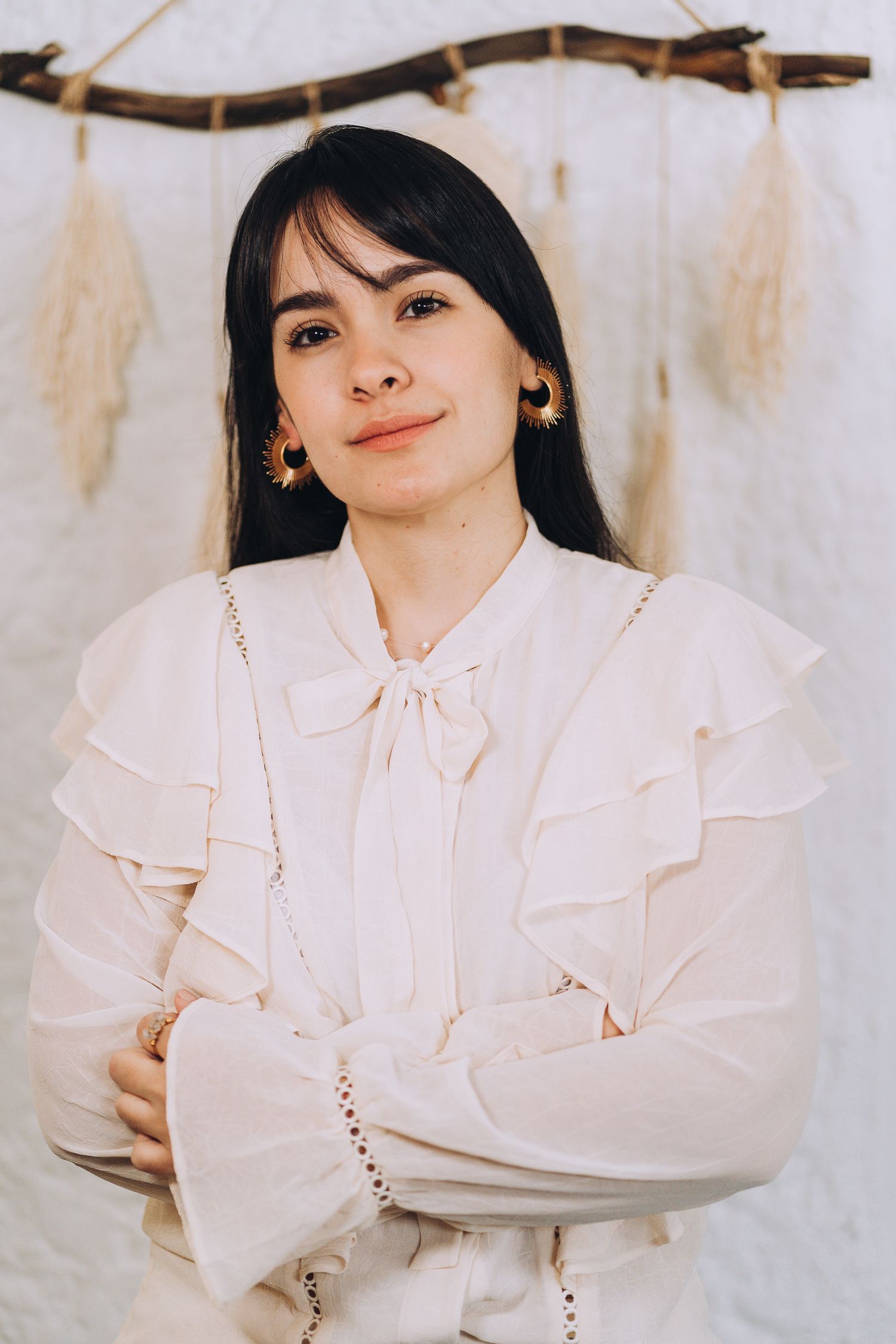 Portrait shot in white ruffled blouse against cream background with rustic branch decor.