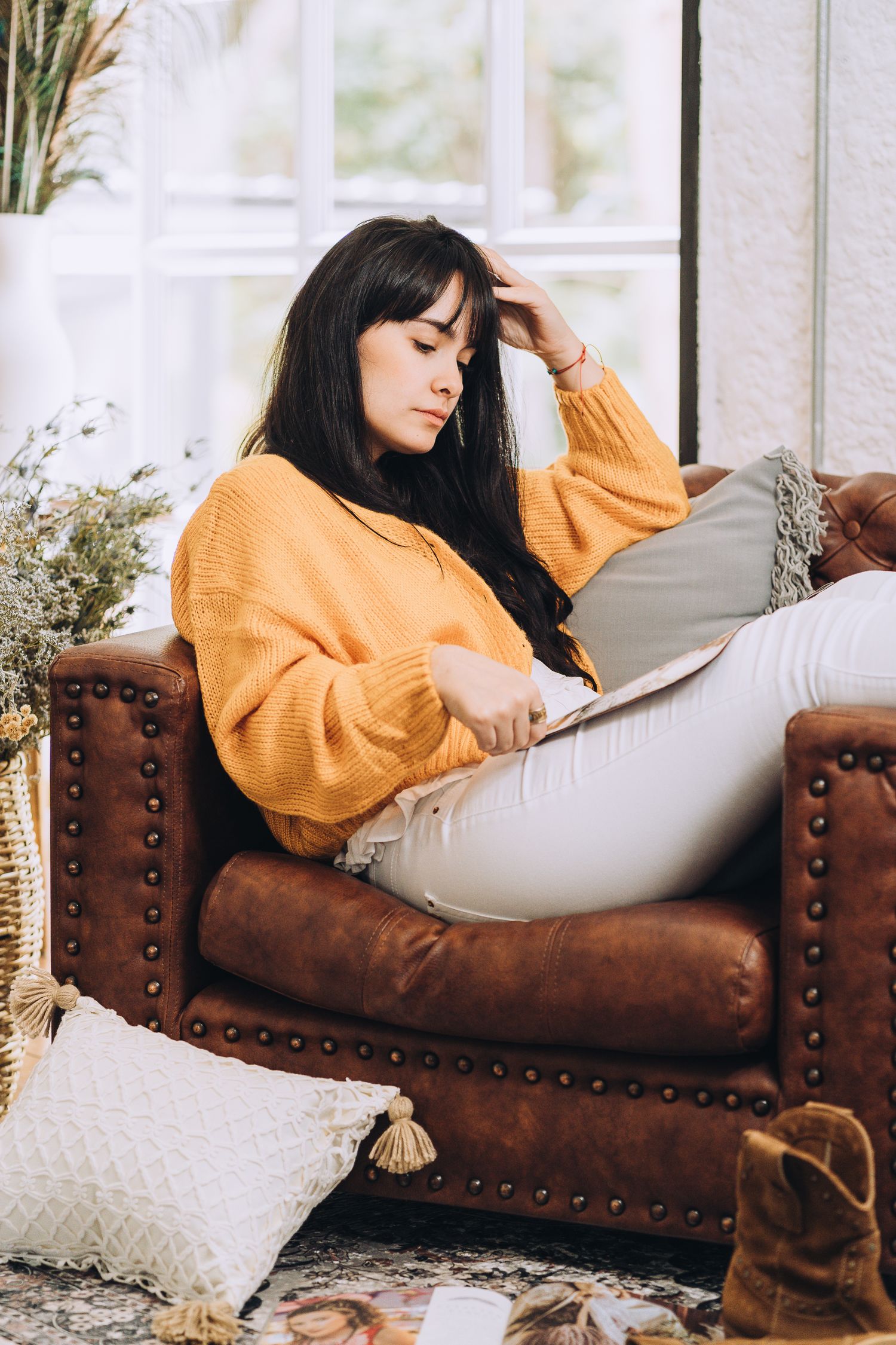 A cozy scene showing someone relaxing in a brown leather armchair wearing an orange sweater while reading.