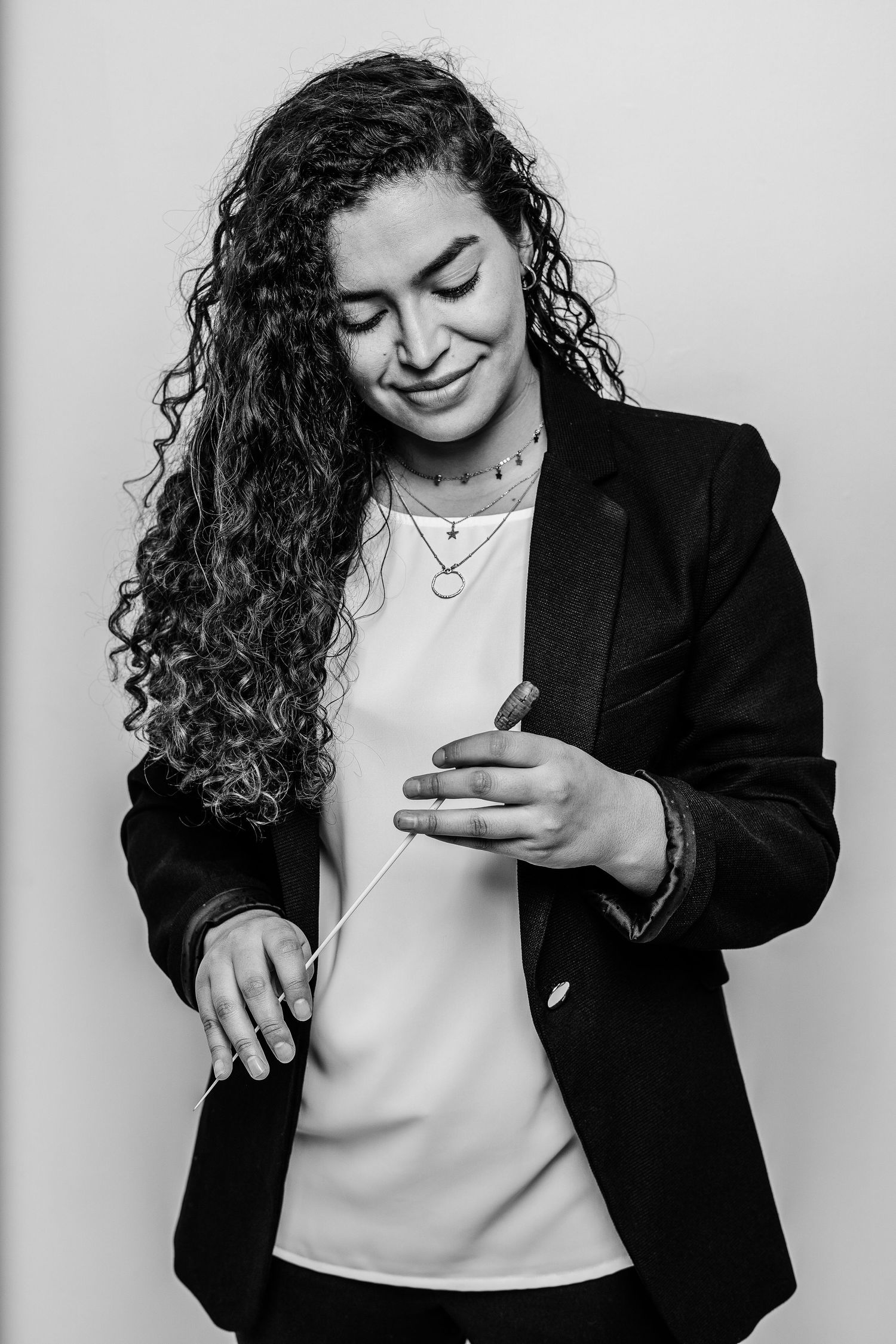 Professional conductor with curly hair in blazer smiling with eyes closed.