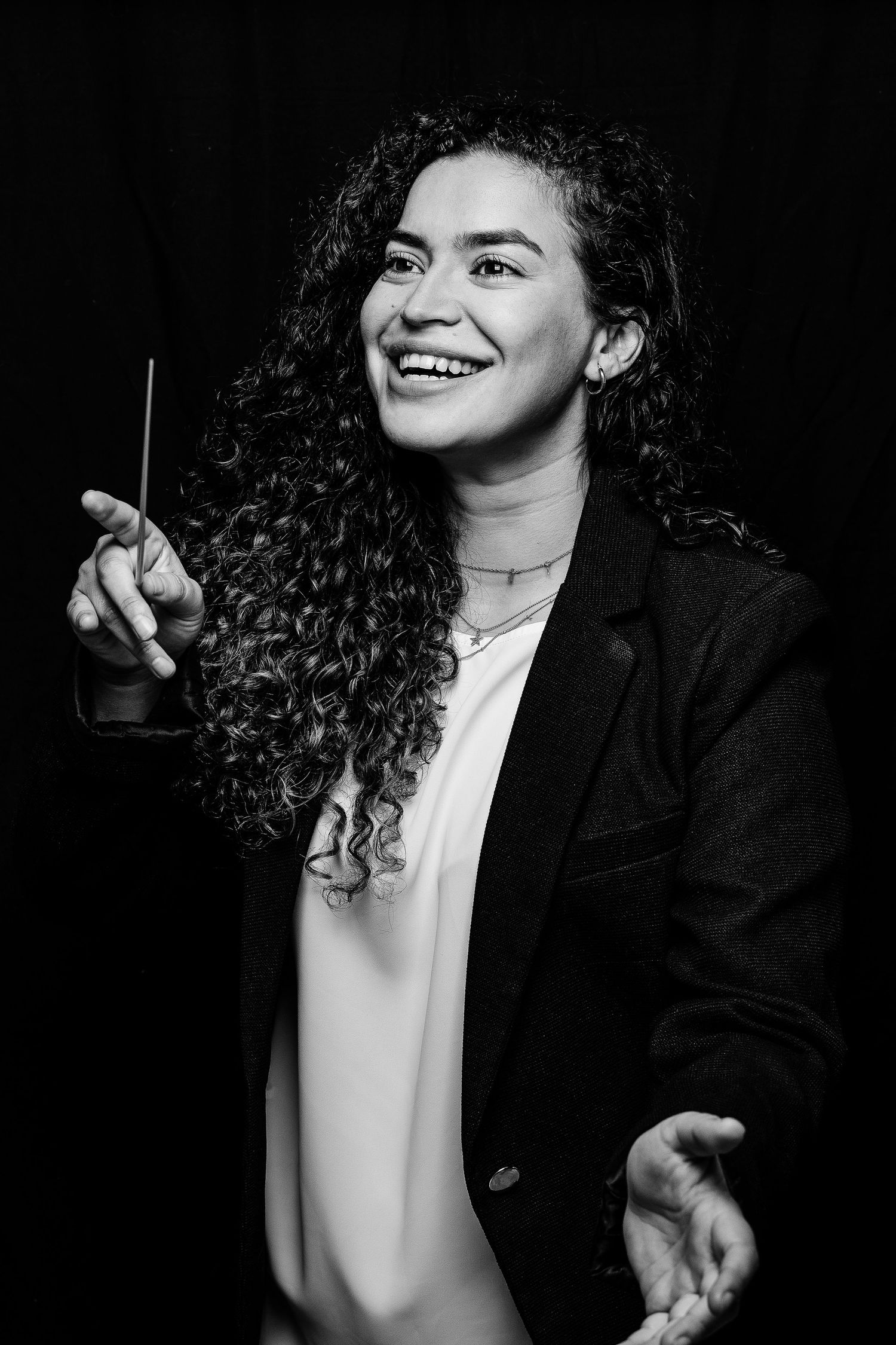 Joyful conductor with curly hair holding baton in black and white portrait.