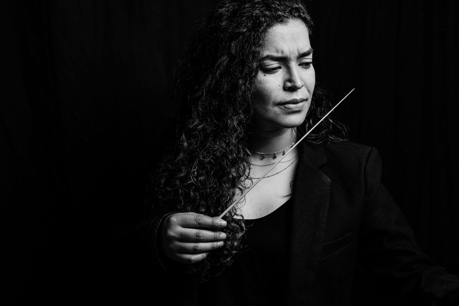 Dramatic black and white portrait of a musician holding a conductor's baton in formal attire.