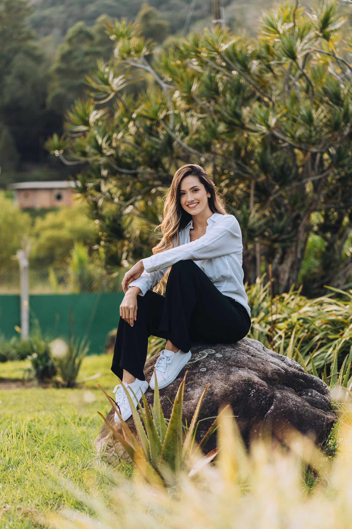 Casual outdoor portrait of someone sitting on rock in garden wearing white shirt and black pants.