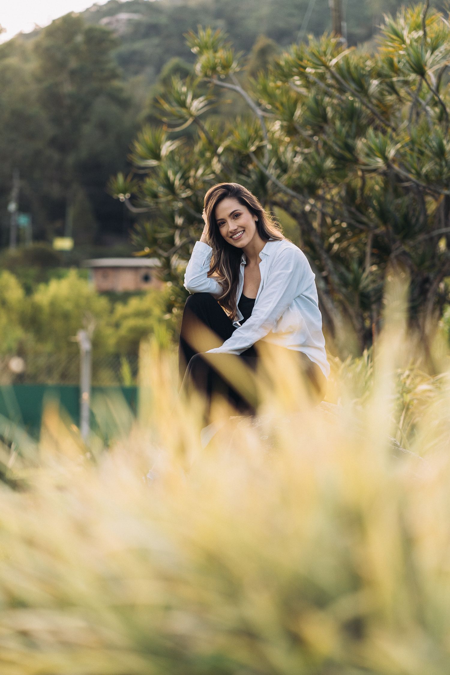 A casual outdoor portrait through tall grass with a green garden backdrop.