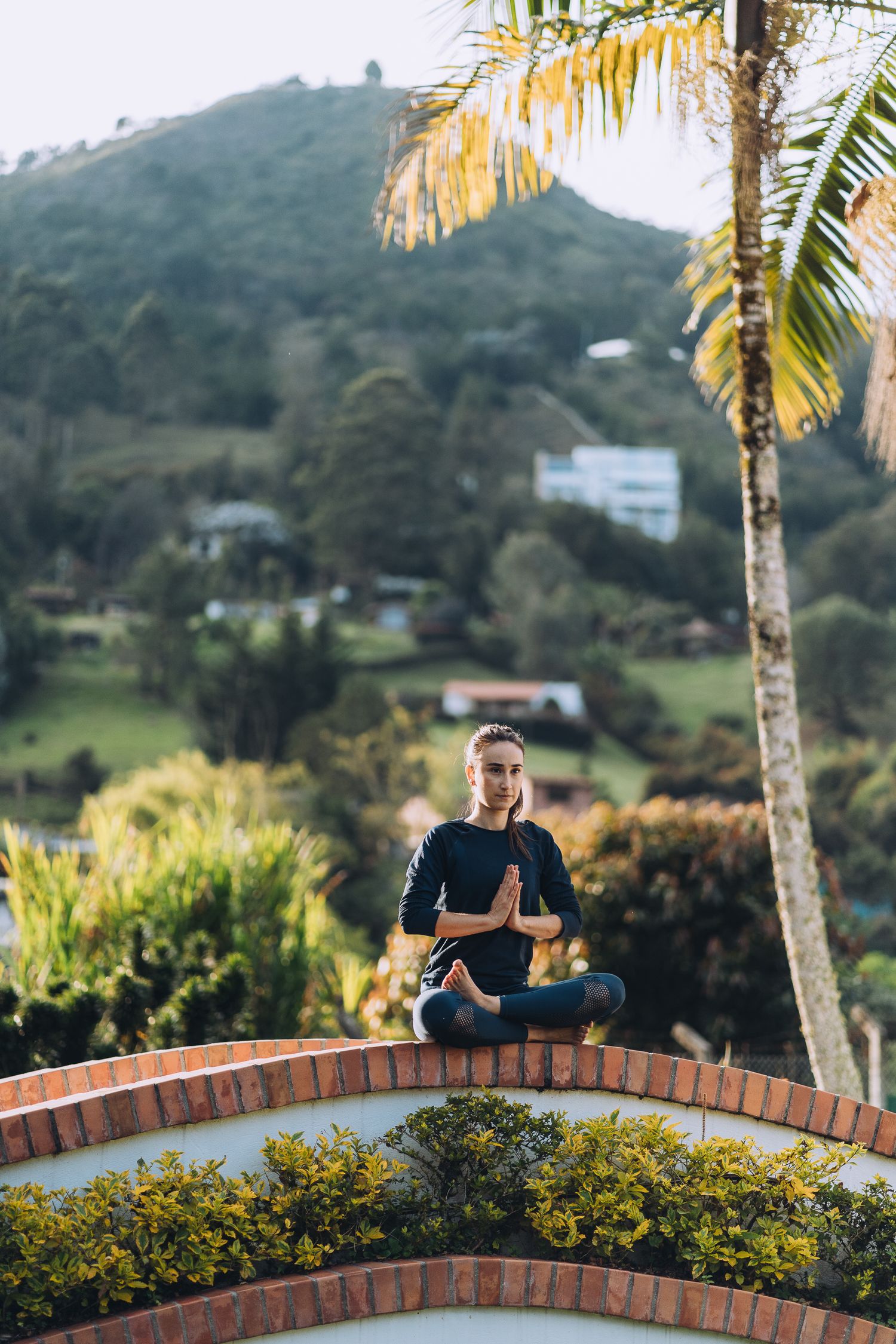 Person practicing yoga on a brick wall with tropical mountain landscape in background.