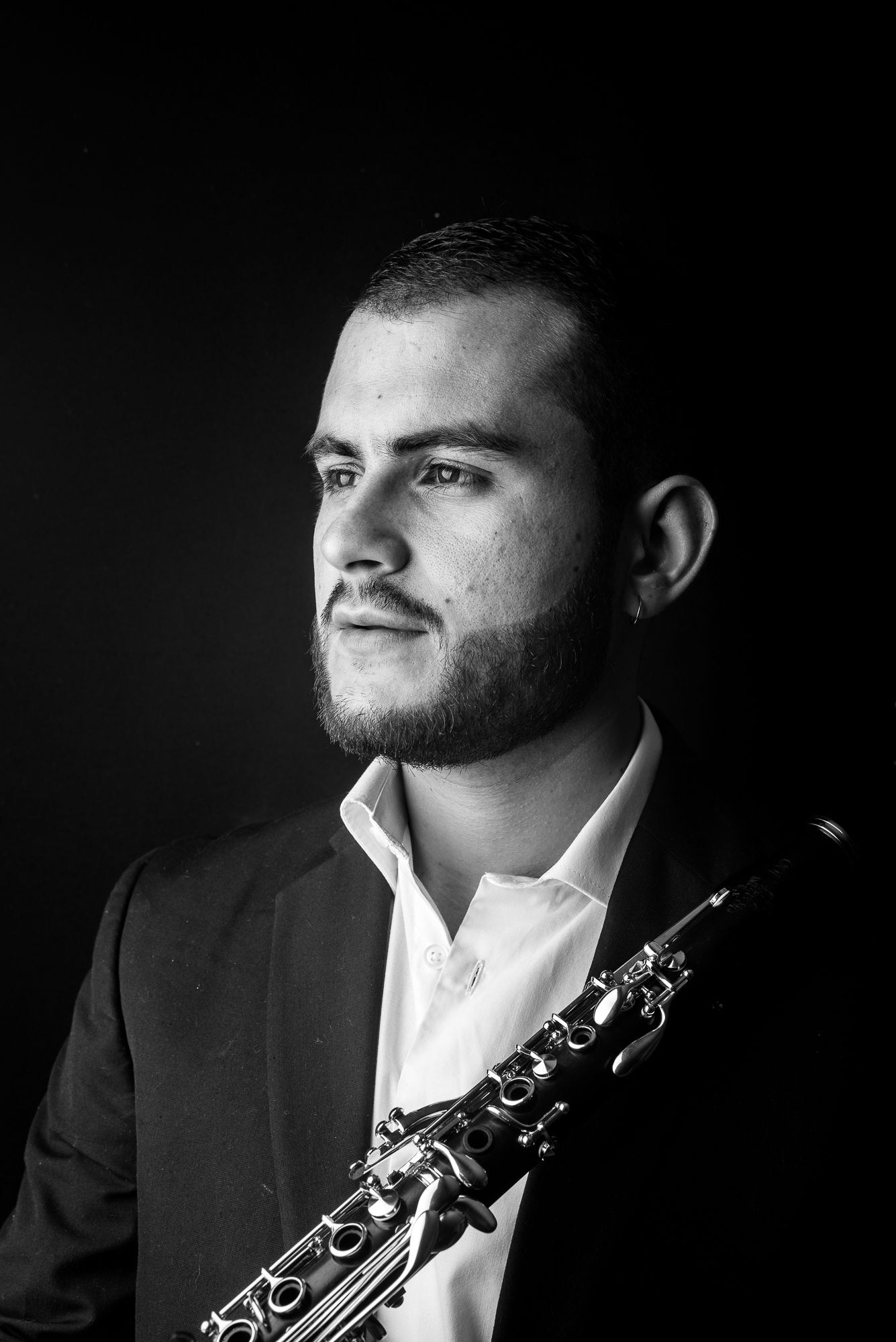 Dramatic black and white portrait of musician holding clarinet against dark background.