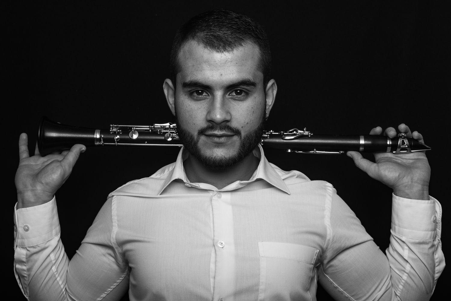 Black and white portrait of musician holding clarinet across shoulders in studio setting.
