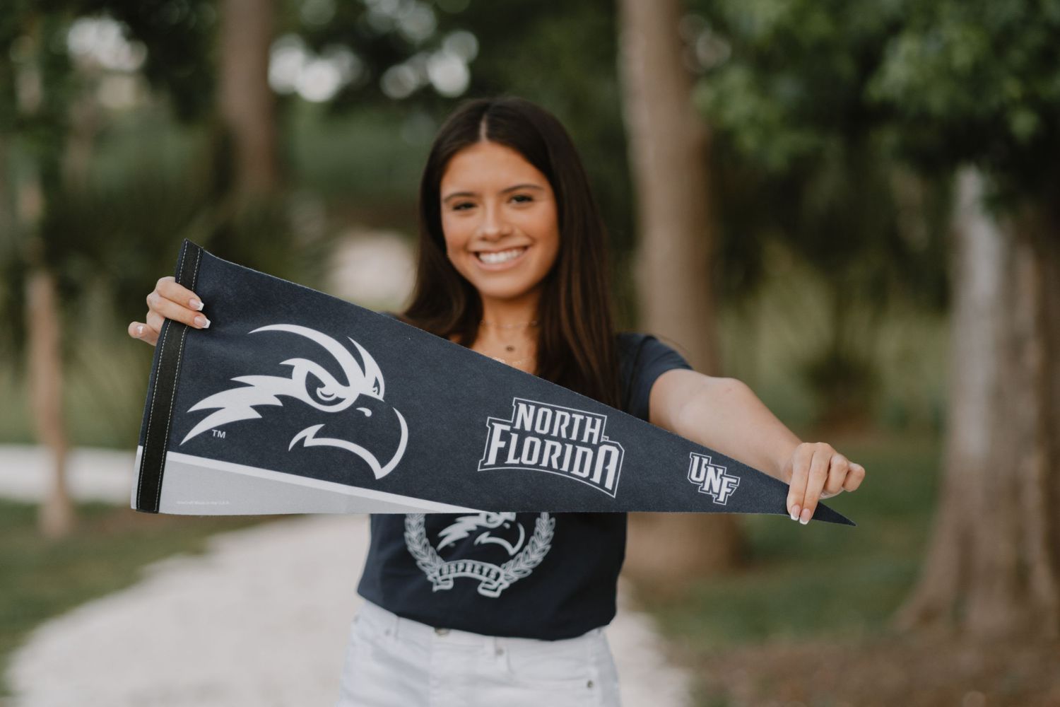 Enthusiastic student shows off North Florida university gear and spirit scarf while posing outdoors on campus.