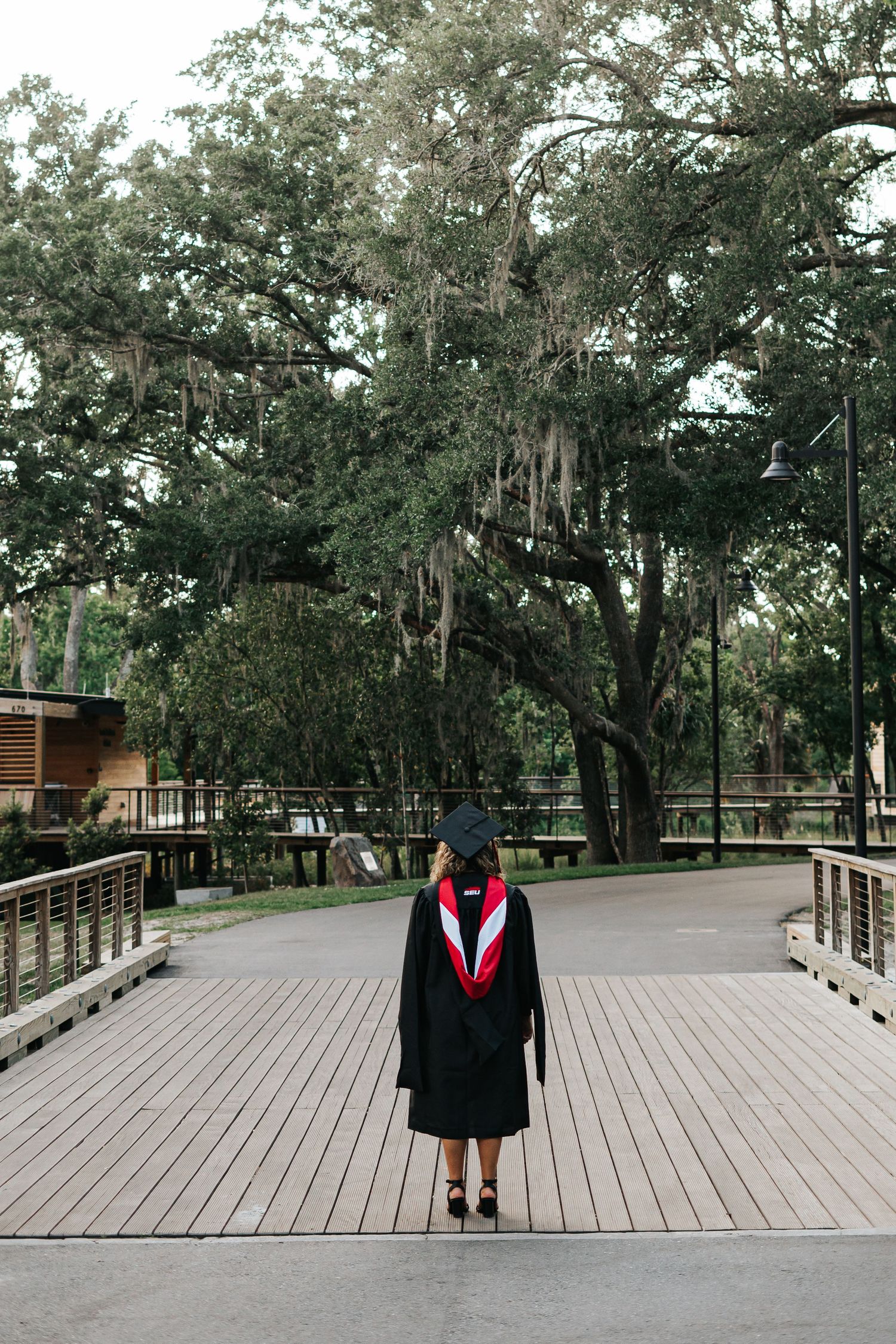 A graduation photo on a wooden boardwalk path surrounded by Spanish moss-draped oak trees.