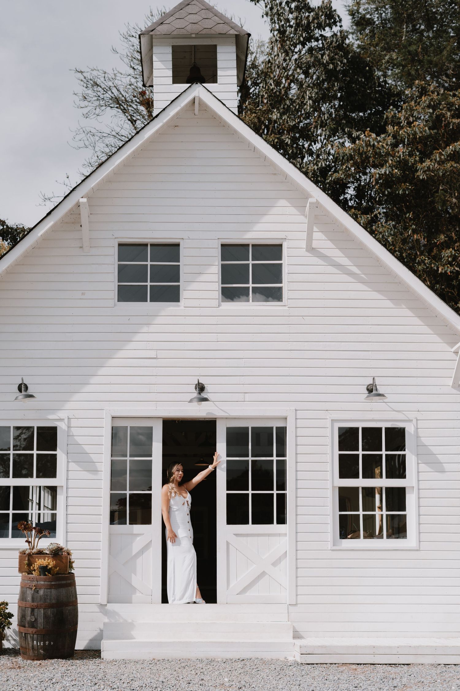 White barn-style wedding venue with rustic details and a decorative barrel by the entrance.