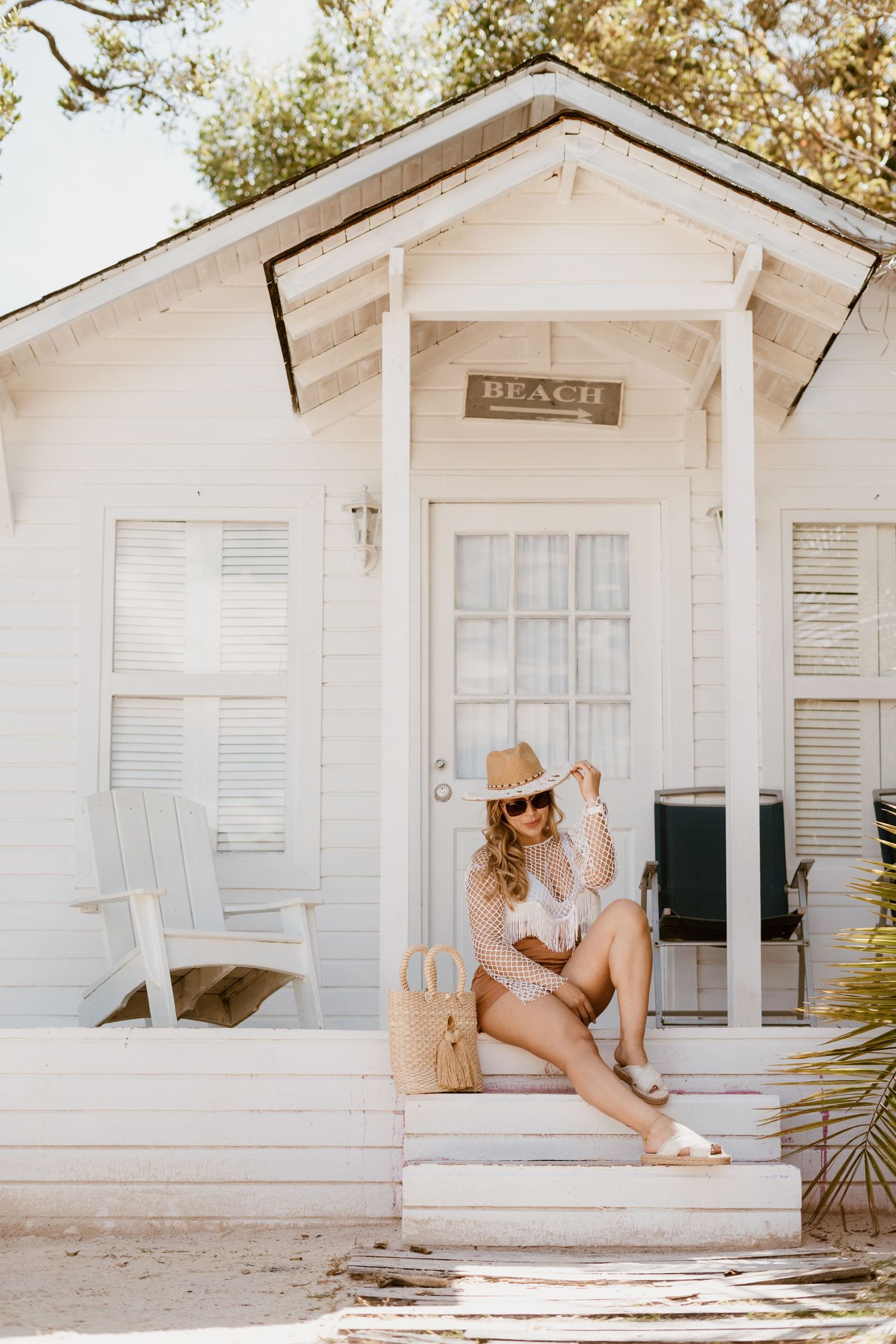 White beach cottage with shutters and rustic 'BEACH' sign above the entrance.