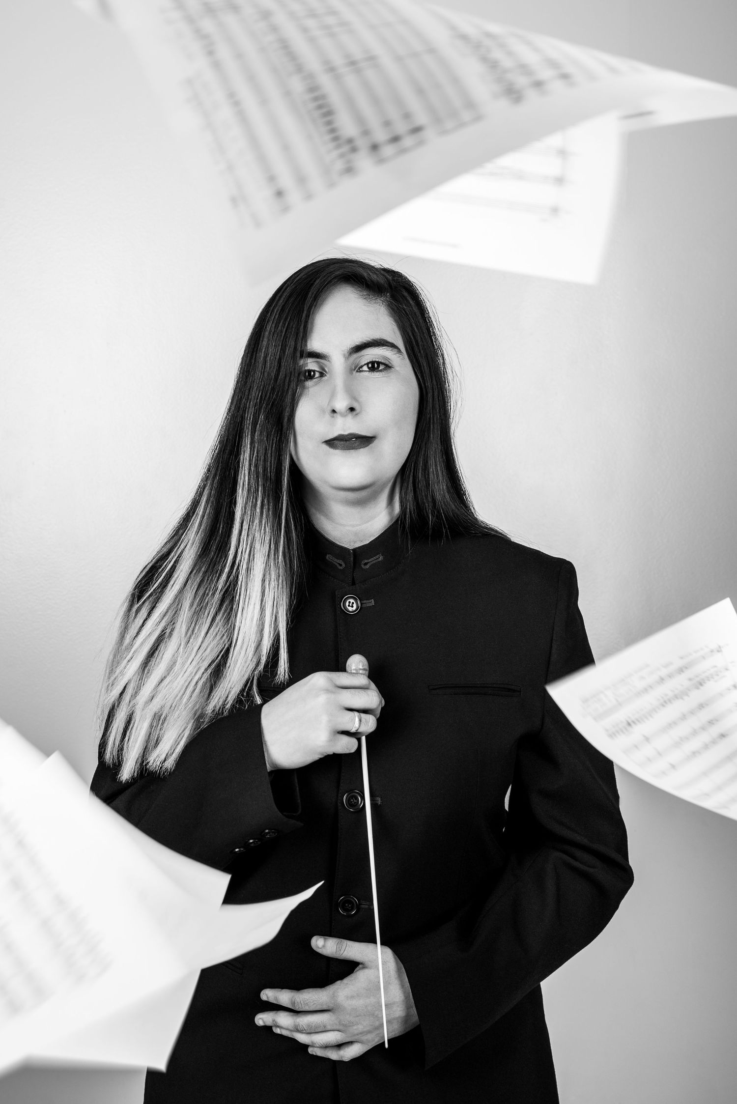 Artistic portrait of a conductor with sheet music flying through the air in black and white.