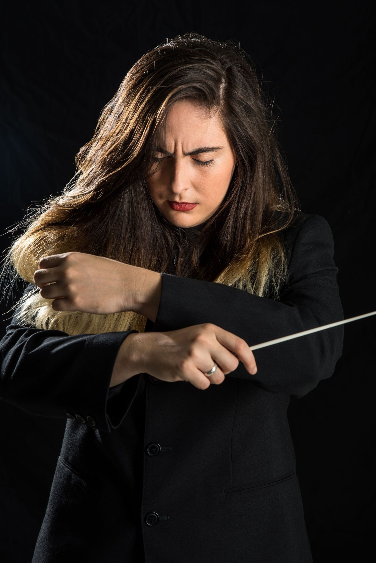 Dynamic shot of a conductor in black attire expressing passion while directing with baton.