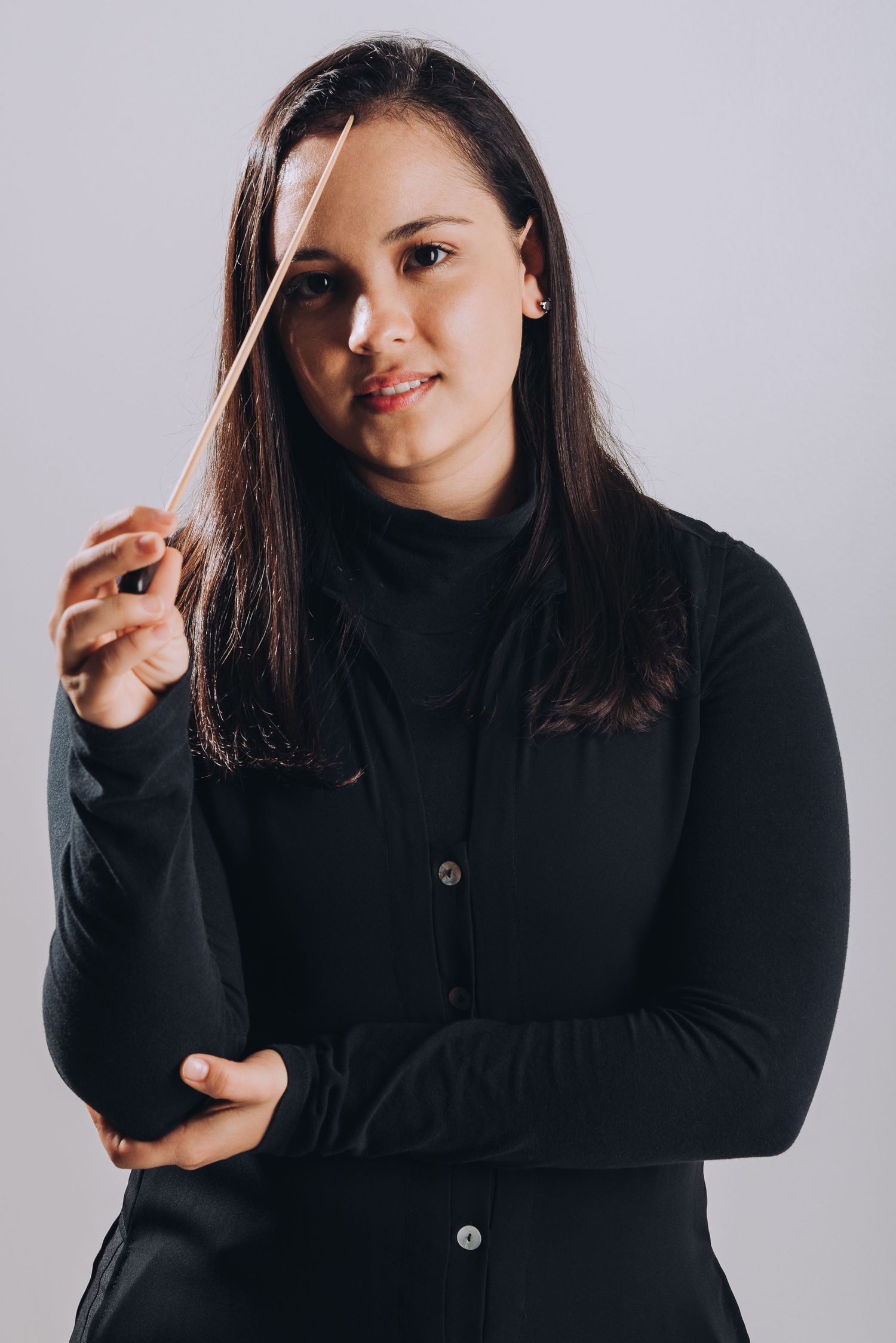 Professional studio portrait of a conductor holding baton against light background.