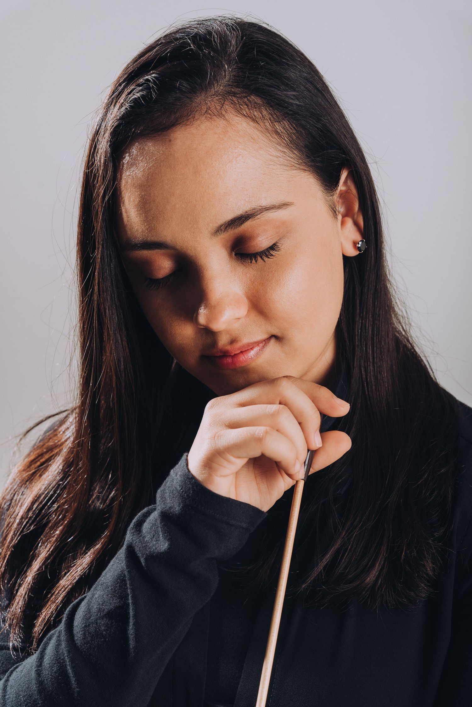 Intimate portrait of a conductor in contemplative pose with baton and black attire.