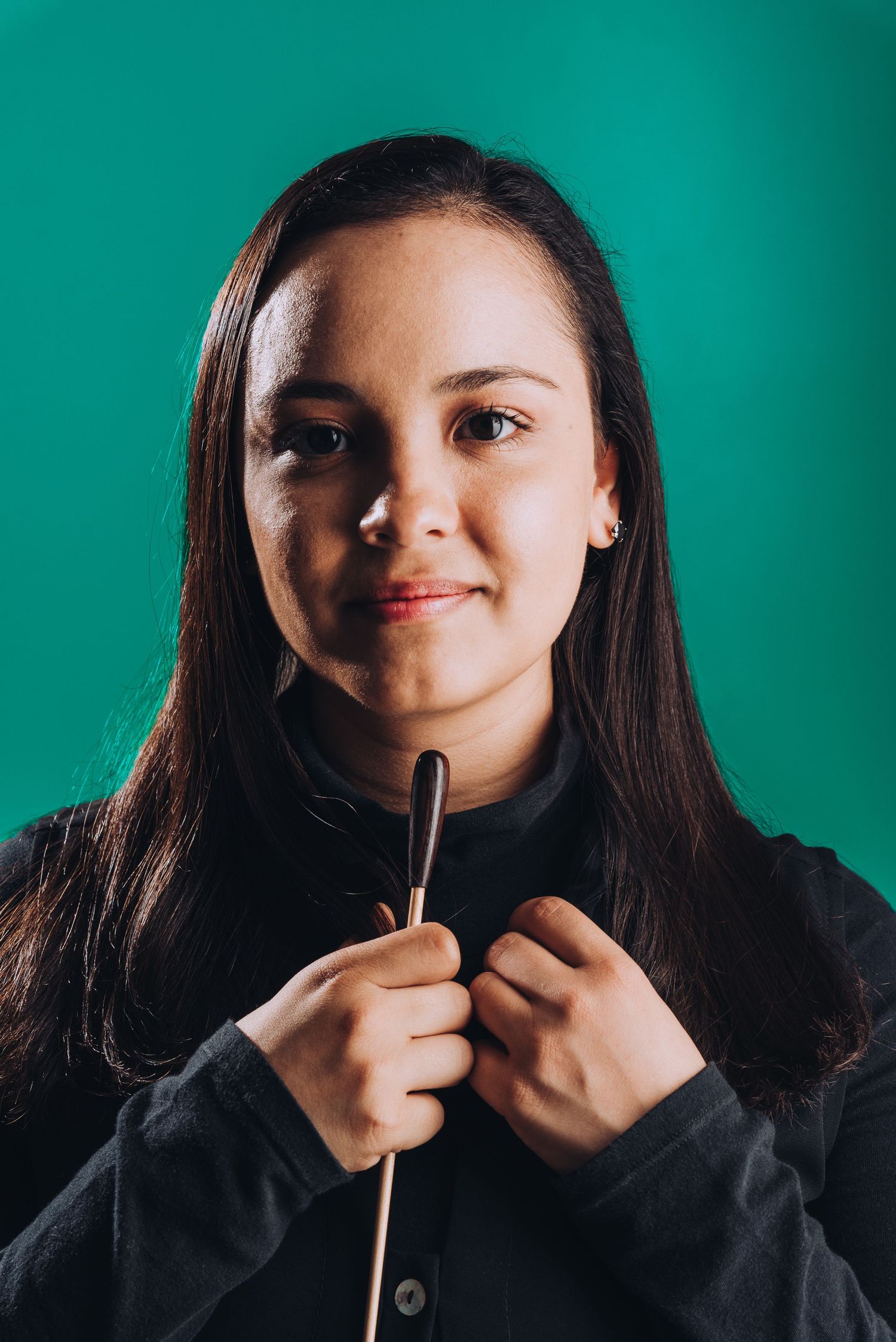 Portrait of a music conductor against vibrant green background holding baton with confident expression.
