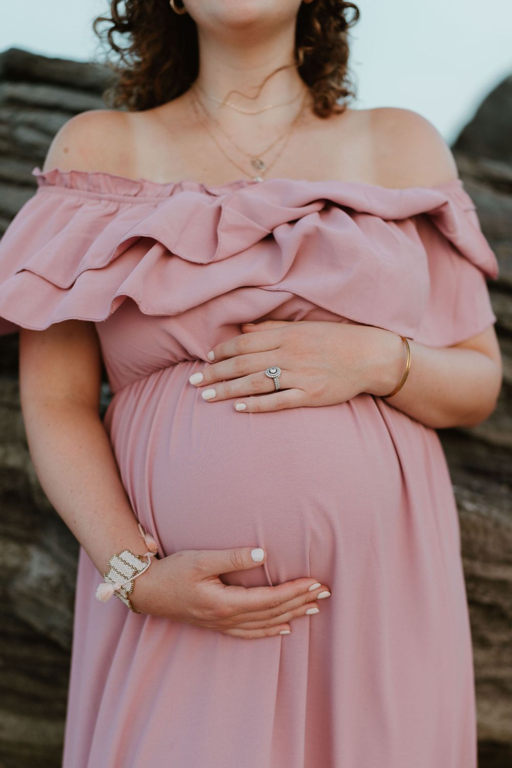 Close-up of pregnant woman in pink off-shoulder dress showing engagement ring.