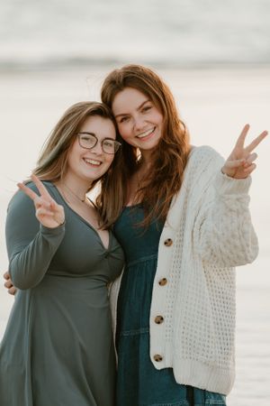 Two friends making peace signs while posing together at the beach.