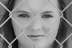 Black and white portrait through a chain link fence creates artistic geometric pattern with dreamy expression.