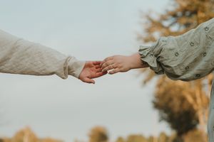 Two hands reaching towards each other against a soft autumn background in gentle muted tones.