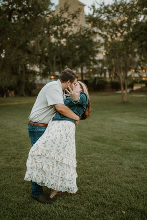 A romantic couple embraces and kisses in a grassy park during golden hour.