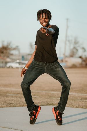 Person in casual attire striking dynamic dance pose outdoors against urban background.