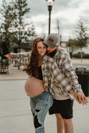 A couple in casual attire shares playful moments together on an urban sidewalk on an overcast day.