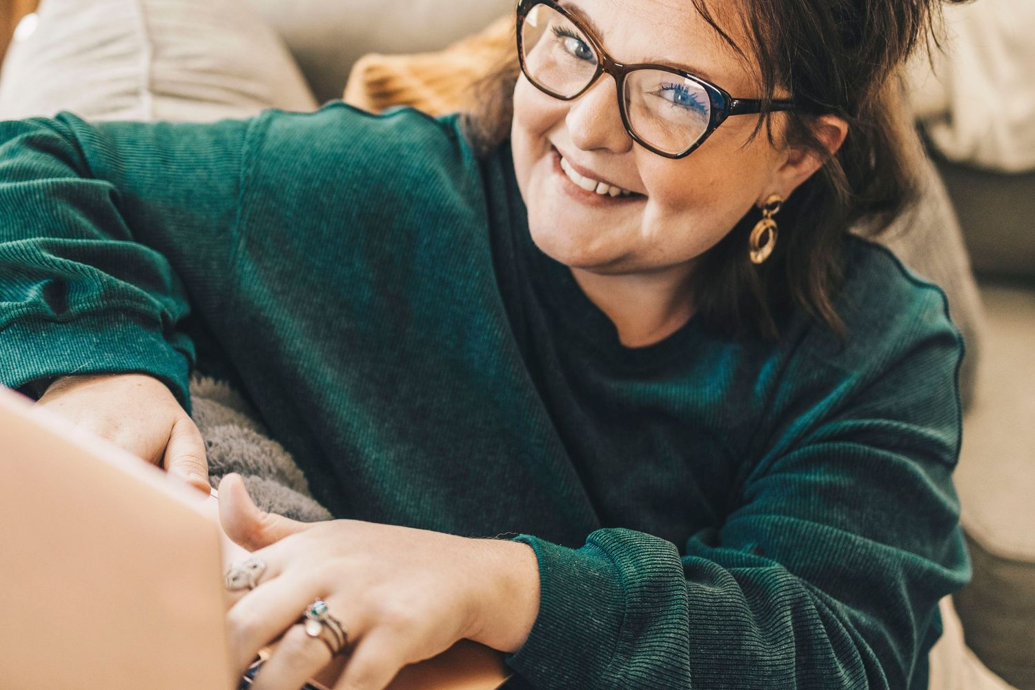 Close-up of smiling woman with glasses using laptop on cozy couch.