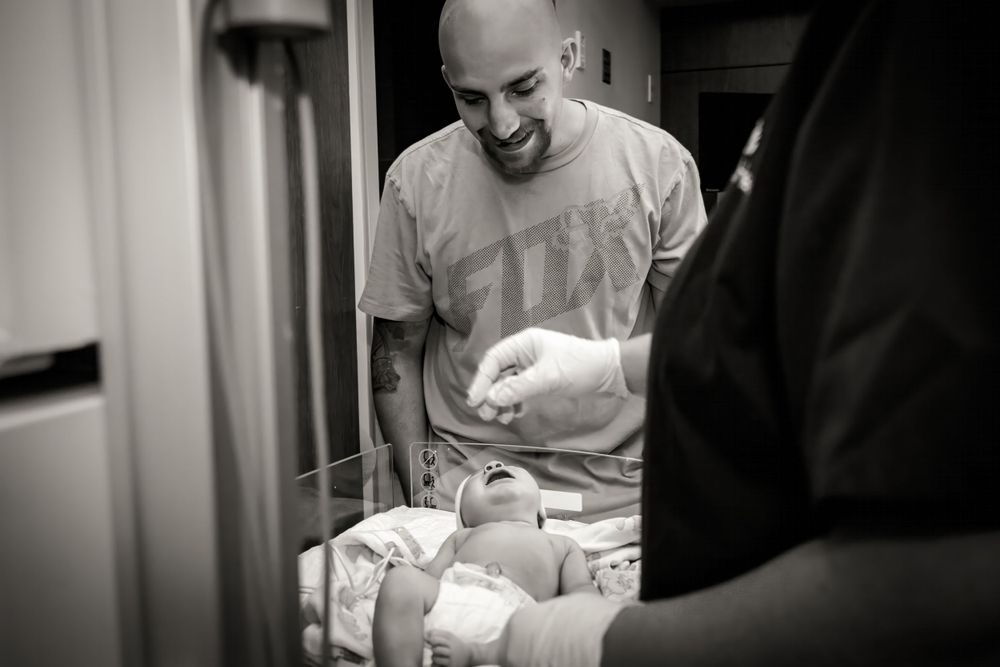 New parents examine their newborn baby in a hospital room.
