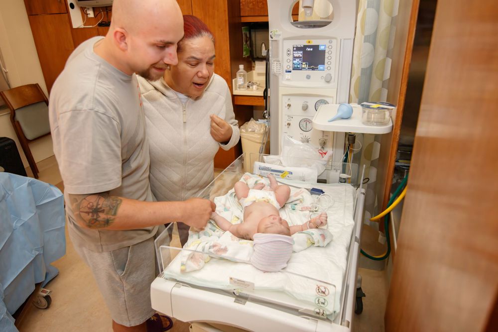 Parents looking down at their newborn baby in hospital bassinet.