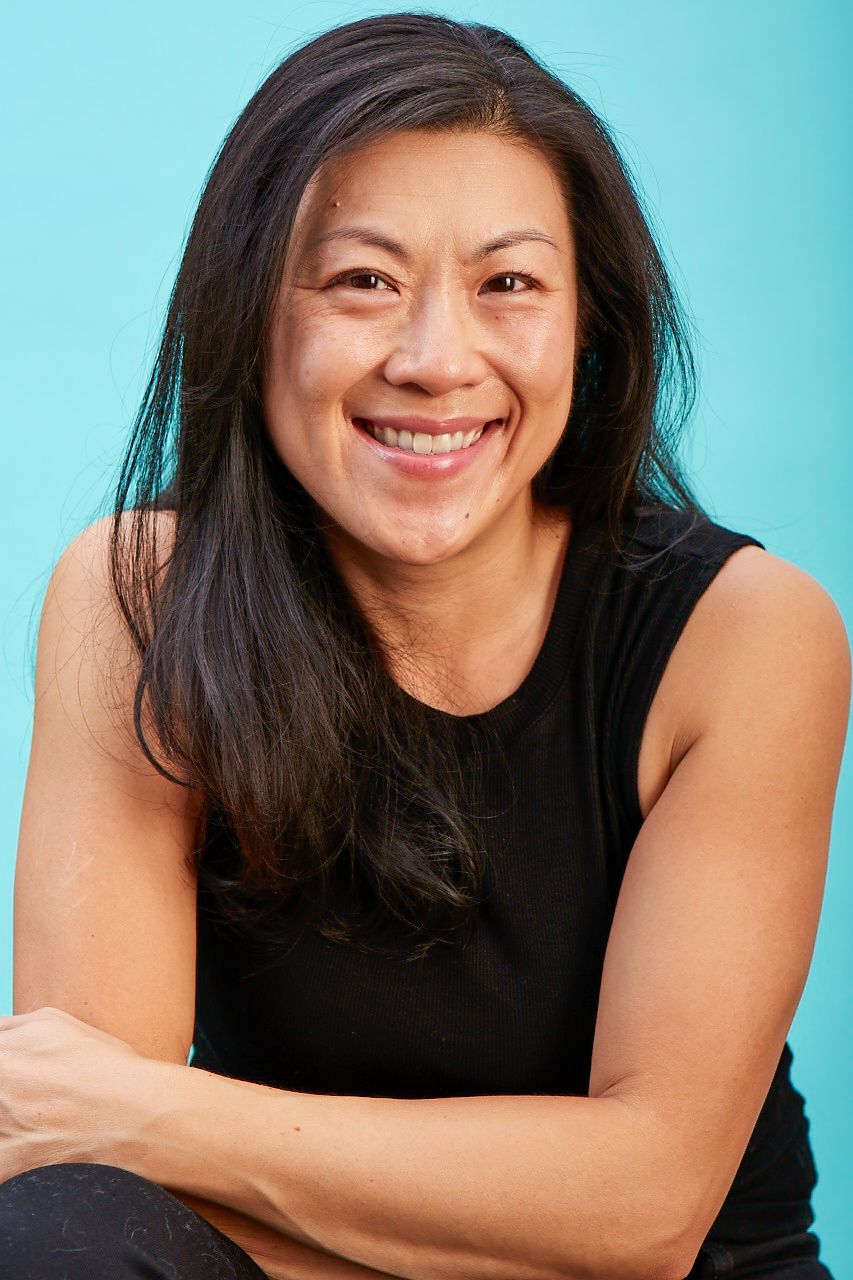Professional headshot against turquoise background showing warm smile and black sleeveless top.