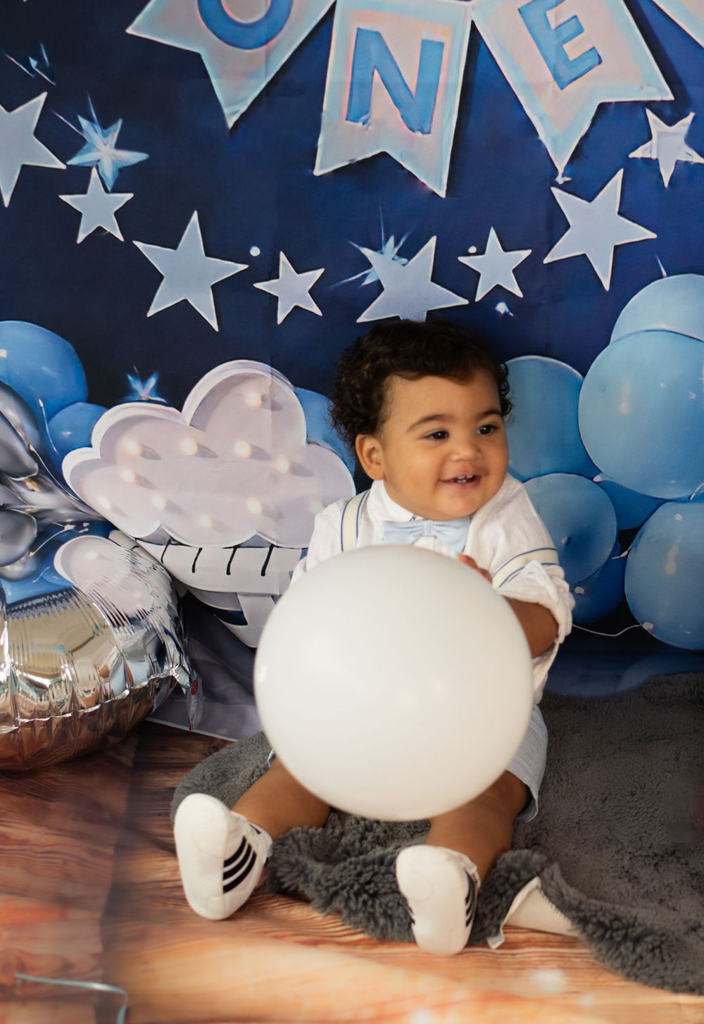 Happy baby playing with white balloon during first birthday photoshoot with blue star decorations.