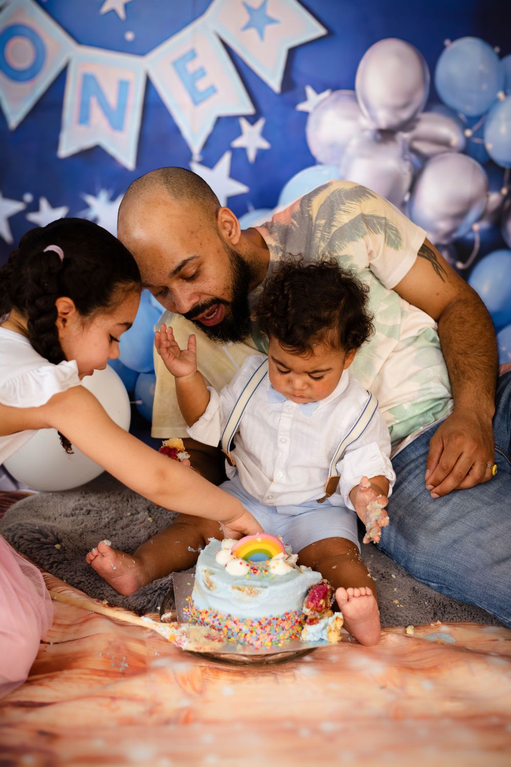 Family gathered around decorated birthday cake during cake smash photoshoot.