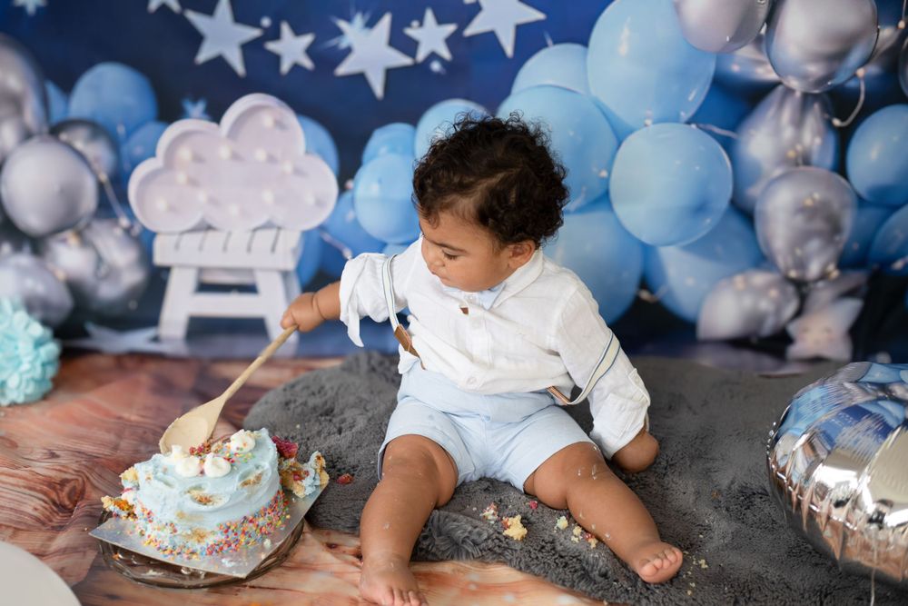 Baby in white outfit exploring smashed cake during first birthday photoshoot.