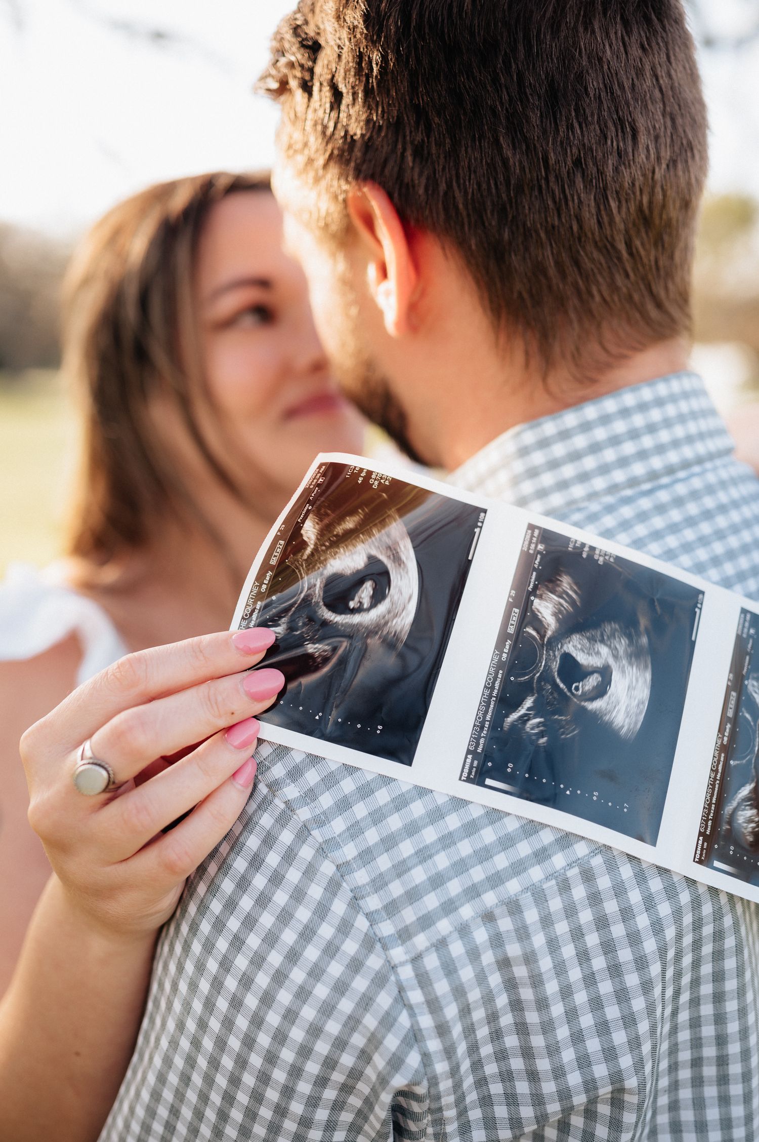 A couple looks at ultrasound images together in warm outdoor lighting.