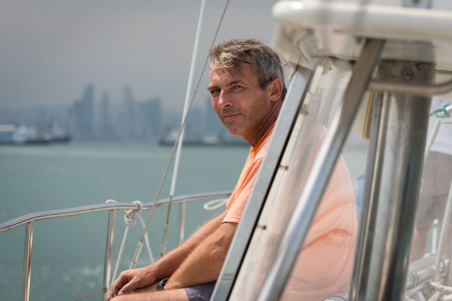 A person in an orange shirt relaxing on a boat deck with a cityscape in the background.