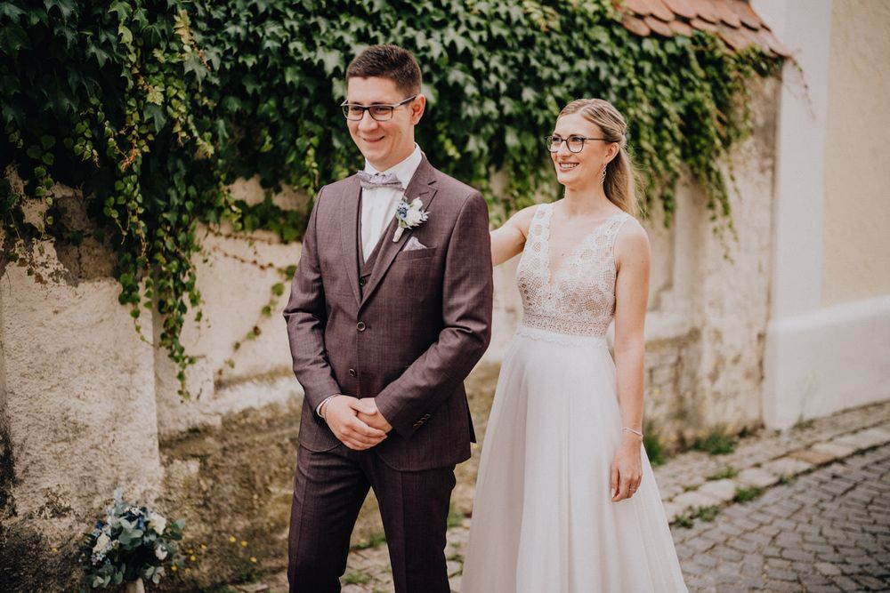 Wedding portrait on cobblestone street with bride in lace gown and groom in brown suit.