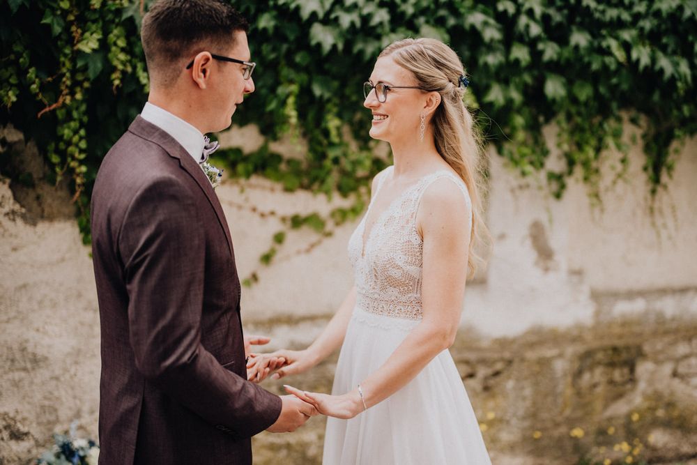 An intimate wedding moment between a couple in glasses sharing loving gazes and holding hands.