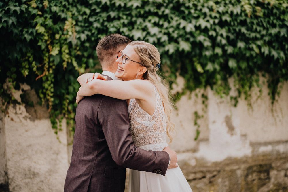 A tender embrace between newlyweds in front of an ivy-covered stone wall.