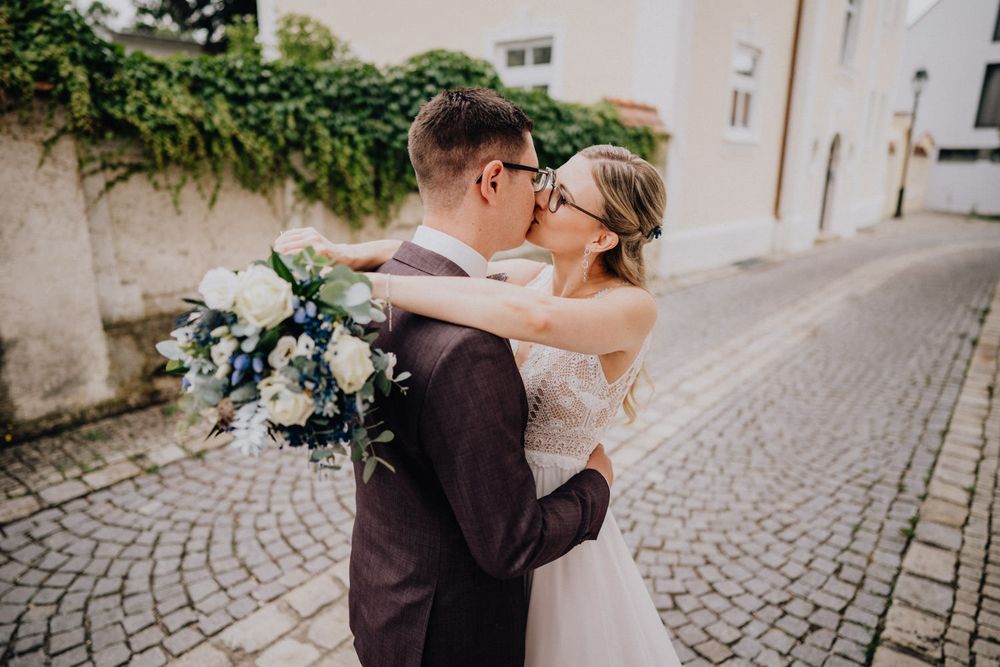A joyful wedding kiss on a charming European cobblestone street.
