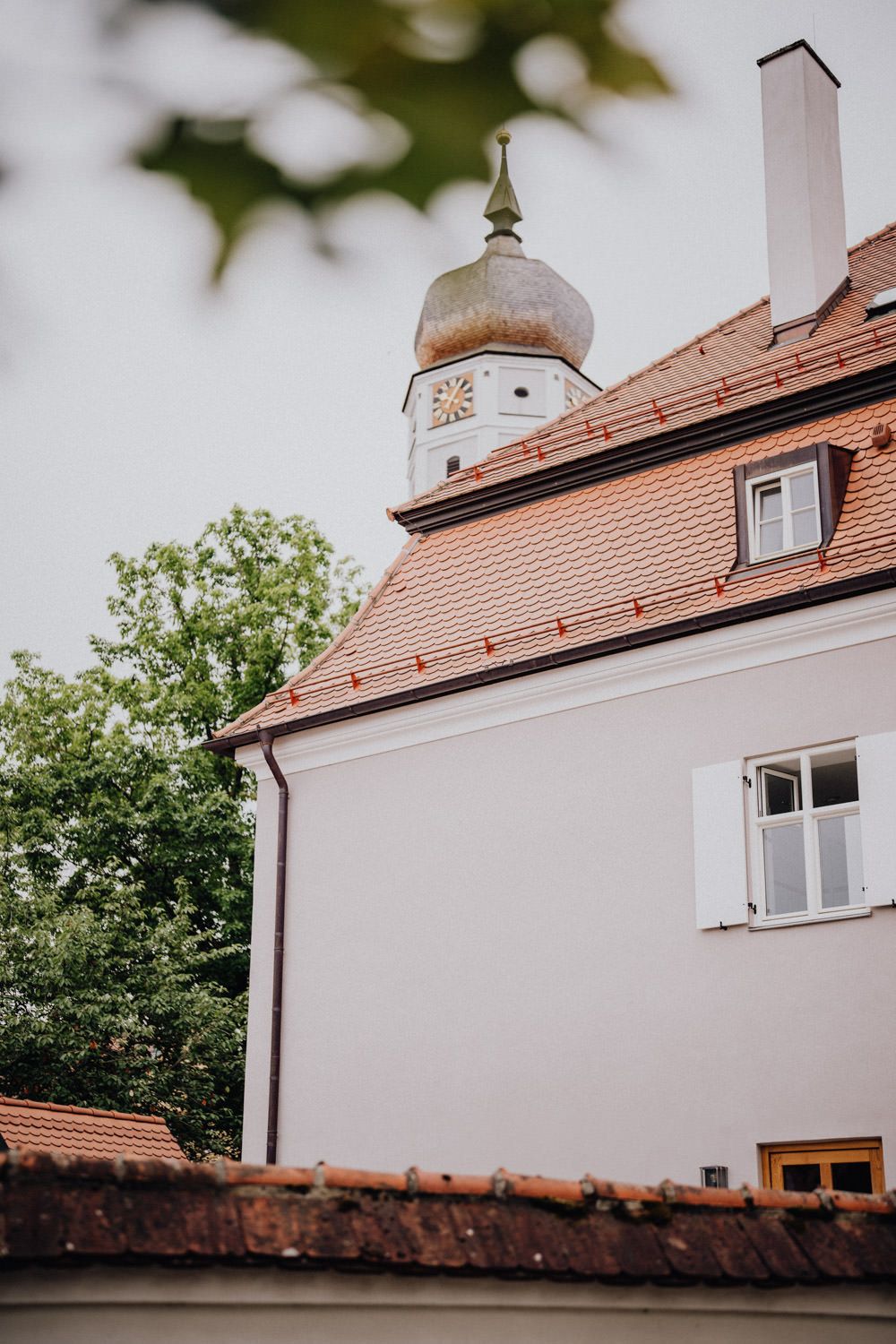 White church tower with copper dome and clock face against blue sky and red tile roof.