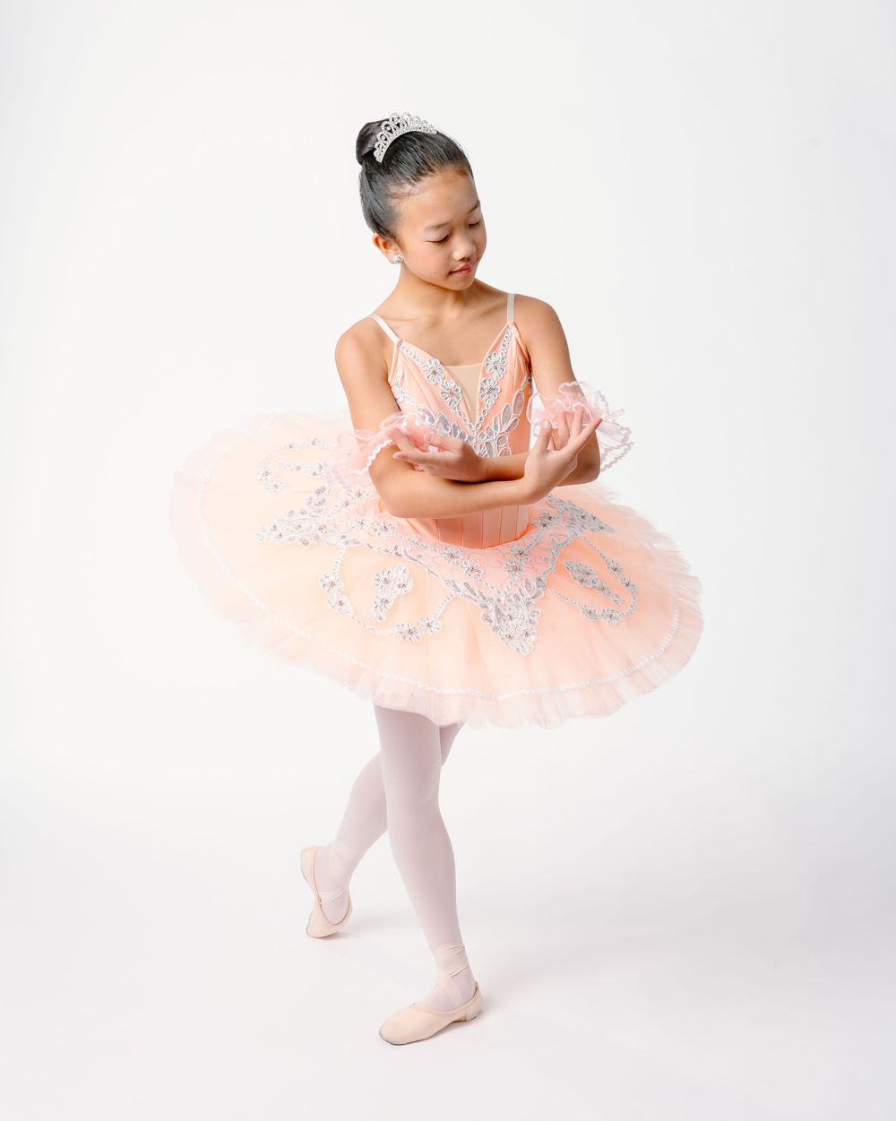 Young ballet dancer in pink tutu performs graceful poses against white background.