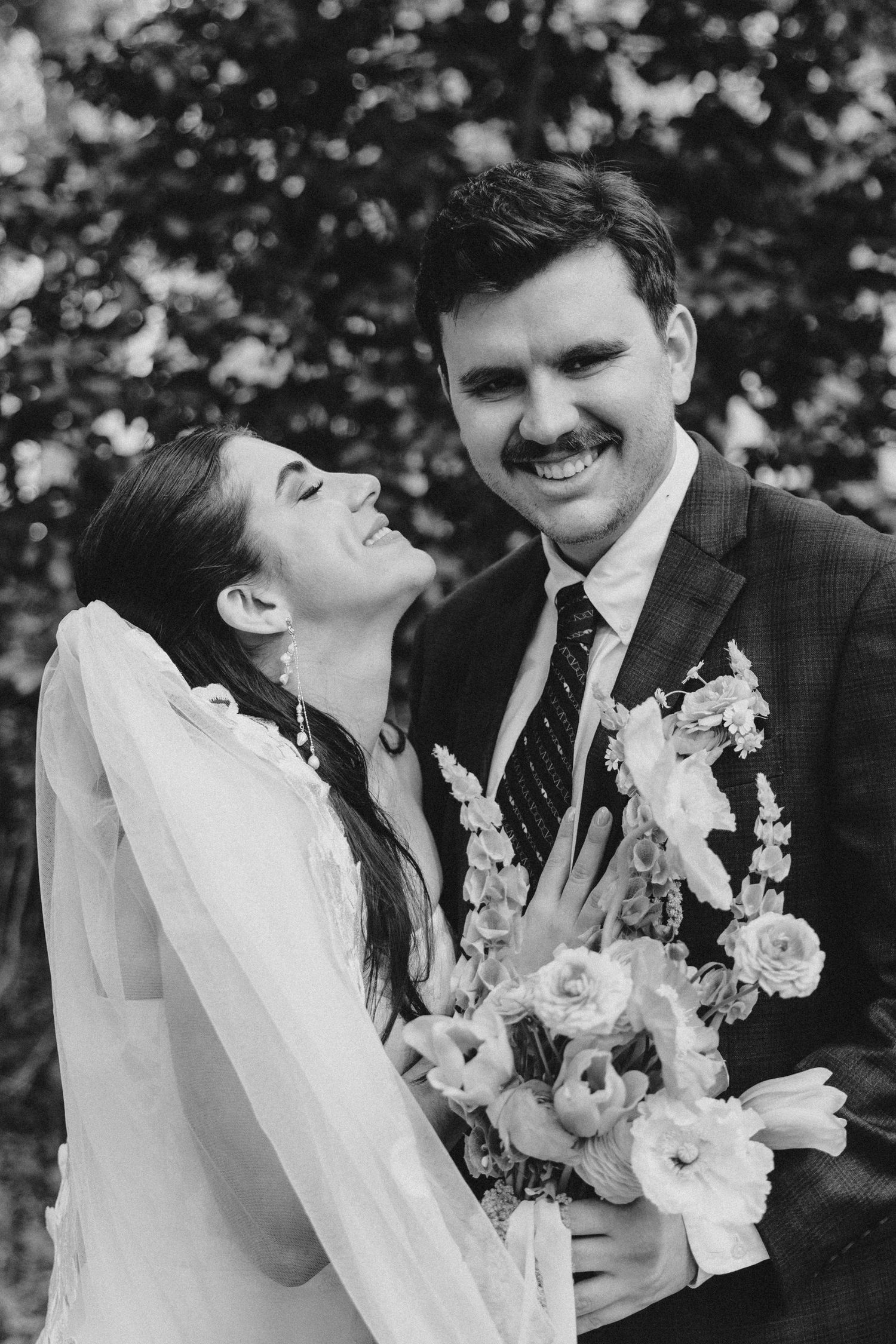 Black and white image of a bride lying back into her groom's lap at Forsyth Park. Her bouquet lays atop her dress's train