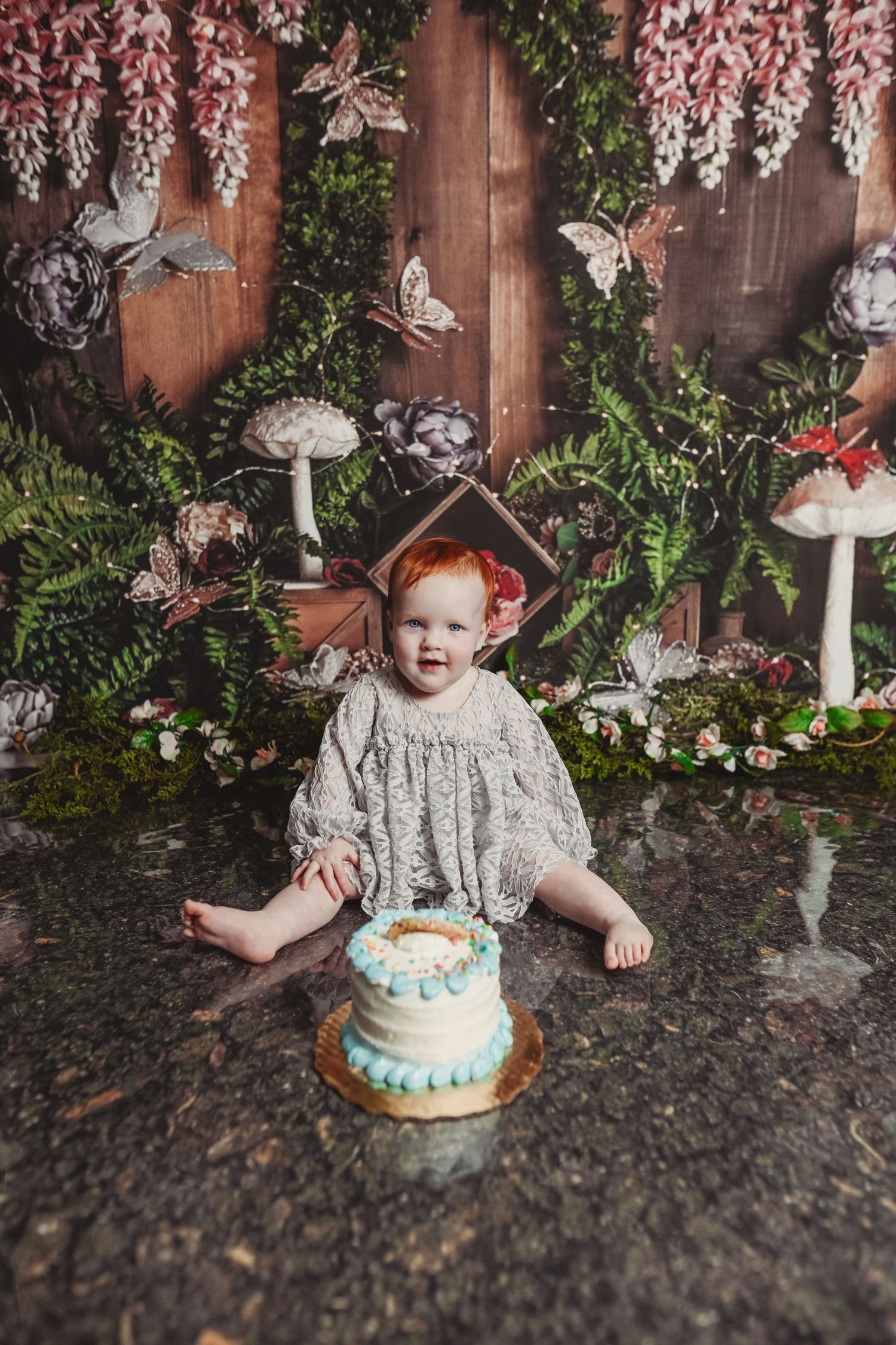 Whimsical fairy garden photo session with decorative mushrooms and a small cake on dark ground.